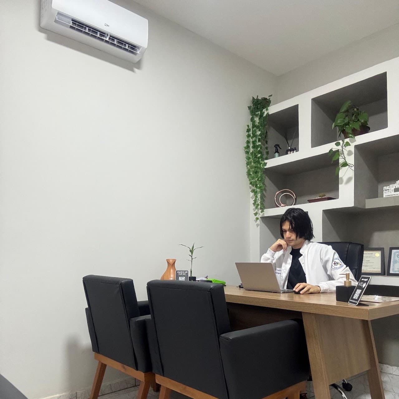 Sala de atendimento - Dr. Willian em atendimento, mesa, poltronas em courino preto e armário de nichos em alvenaria